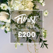 In a bright, studio-like light, a lush white-and-cream floral spray centers the frame, an offering from Flowers Mill Hill to the Mill Hill community. The heart of the arrangement is built on ivory roses, some unfurling to reveal velvety petals, others still nurtured in tender buds, their creamy glow blending with generous clusters of hydrangeas that create a cloudlike mass. A cascade of elongated white blooms, resembling sweet peas, threads downward with graceful ease, their stems carrying a soft motion that suggests movement in a gentle breeze. Interspersed among the florals are white Nigella, Love-in-a-Mist, with distinctive green centers and feathery seed heads, adding architectural charm and a touch of whimsy. The greens are varied and lush: broad, deep-green leaves form a sturdy backdrop, lighter, variegated foliage gives subtle contrast, and fine, feathery fronds provide airy dimension. From the base, thin rustic stems peek, contributing to the spray's natural, trail-like finish. Over the central cluster sits a crisp white rectangular frame, within which the text reads Florist Choice in an elegant script at the top, followed by CHOICE SPRAY in bold uppercase, with the price ?200 displayed prominently at the bottom. The background is a soft beige-white that makes the whites sing and the greens glow with vitality. This is a high-quality, versatile spray, ideal for remembrance, celebration, or tribute, and available for same-day delivery across Mill Hill and nearby streets such as Mill Hill Broadway and The Ridgeway. Crafted with care by Flowers Mill Hill, it embodies refined generosity, calm dignity, and timeless elegance.