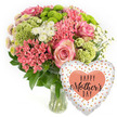 Against a bright, uncluttered white background, this image captures a cheerful Mother's Day flower and balloon gift set, ready to be imagined arriving at a home in Mill Hill. The clear glass vase at the centre is filled with water and showcases a tidy cluster of green stems supporting a dome-shaped bouquet. At first glance, the pink roses stand out: full-headed blooms with velvety petals that show a subtle shift from softer blush centres to slightly deeper pink rims, giving a sense of warmth and tenderness. Intermingled with these are numerous coral-pink florets that resemble kalanchoe, forming compact, textured clusters that bring a lively, almost playful note to the design. Scattered throughout are lime-green button chrysanthemums, their neat, rounded forms and intricate petal structure lending a crisp, contemporary edge. White daisy-style spray chrysanthemums and similar small white blossoms peek between the more saturated colours, softening the bouquet and adding an airy brightness. Deep green leaves provide a lush backdrop, shaping the arrangement and anchoring its vibrant hues. To the bottom right of the vase, a heart-shaped foil balloon leans into view. Its surface shines softly, with a white or light silver background adorned with irregular polka dots in shimmering gold and pale silver-peach, like tiny festive splashes. In the middle, a peach-coloured heart displays the words HAPPY Mother's DAY in elegant black script and bold type. The overall composition feels joyful, caring, and ready to travel from a local Mill Hill florist to a mother living near Mill Hill East, around the Broadway shops, or in one of the quiet cul-de-sacs that look out over the rolling North London hills.